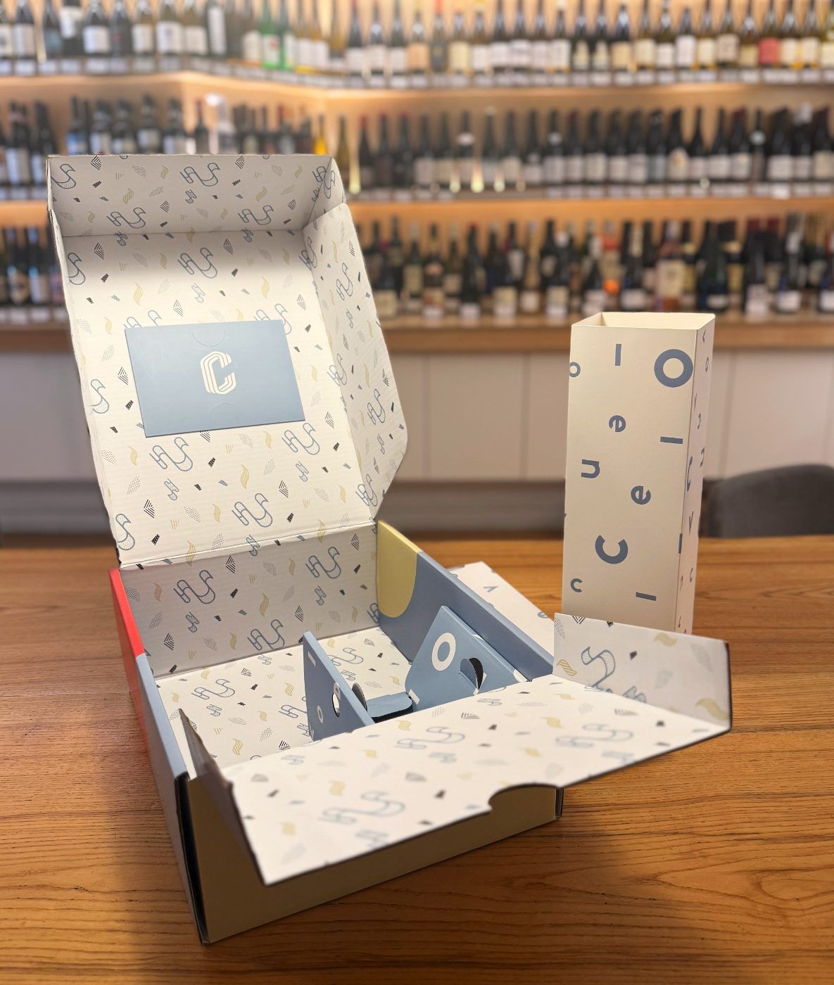 An open gift box with patterned tissue and a tall sleeve covered in scattered letters.
