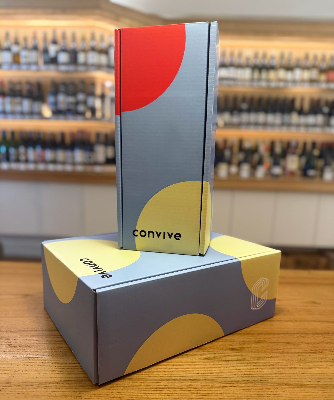 Stacked gray gift boxes with red and yellow circles and the word convive.