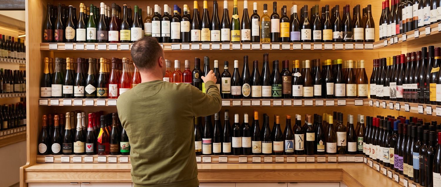 A man seen from behind reaches into a wall of evenly spaced bottles.