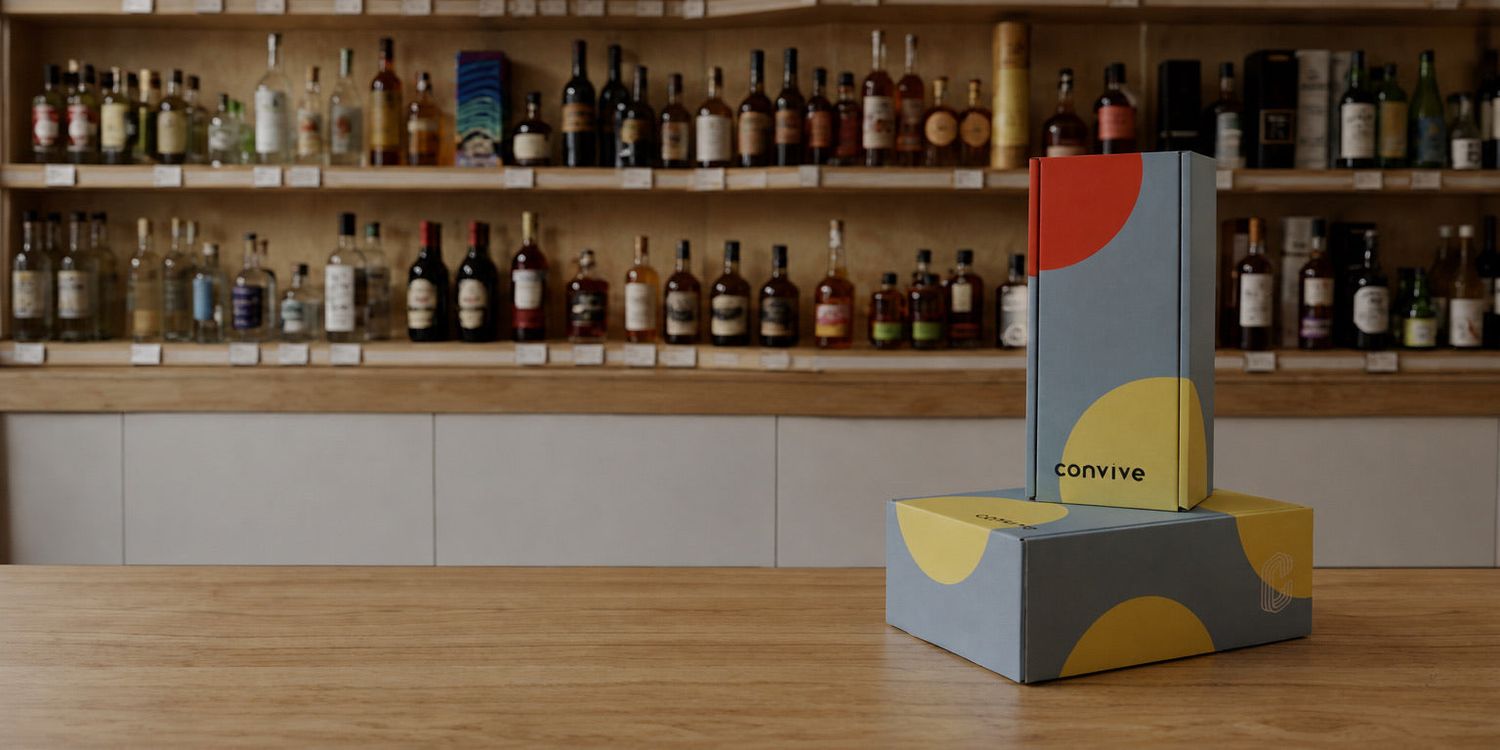 Two gray gift boxes with red and yellow circles and the word convive, on a wood counter.