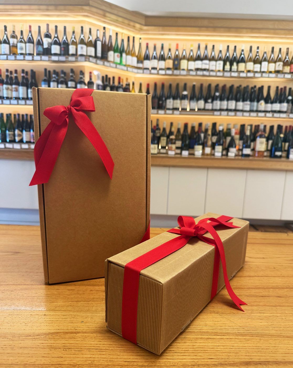 Two kraft boxes tied with wide red ribbon, in front of a generated wine wall.