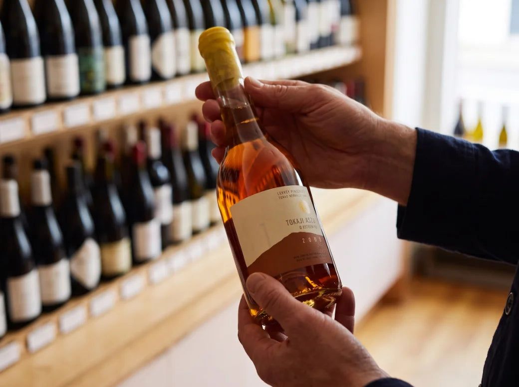 Hands hold a small bottle of amber wine with a generated Tokaji label.