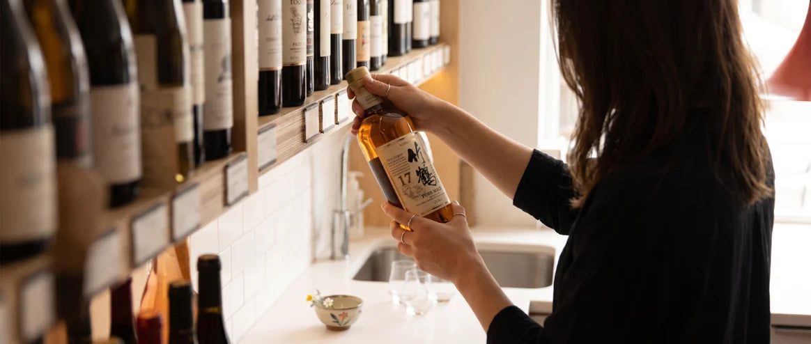 A woman holds a whisky bottle up to a shelf in the generated shop.